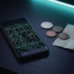 Phone showing a payment code beside unmarked coins, illustrating cryptocurrency checkout for a VPN Safe invoice.